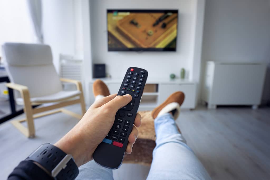 Man watching TV at home Holding remote controller and switching channel First person view - CATANFA